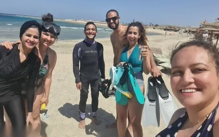Six smiling snorkelers posing together on the beach with fins and snorkel gear after a swim.