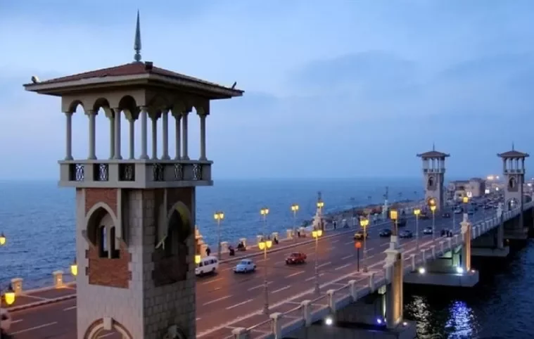Twilight view of Stanley Bridge's ornate towers illuminated along Alexandria's seafront road at dusk.