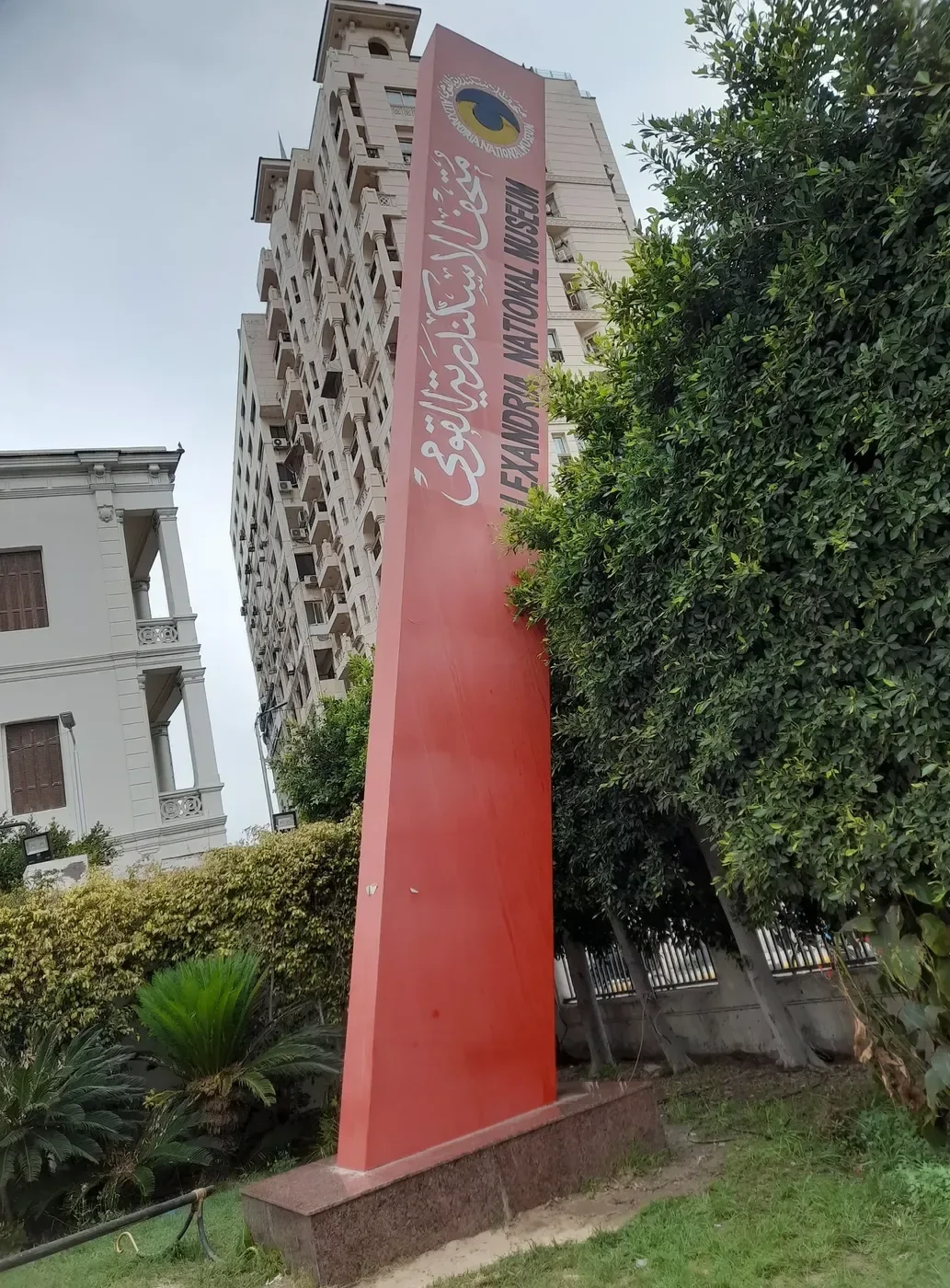 A tall red pylon sign reading Alexandria National Museum in English and Arabic outside the building.