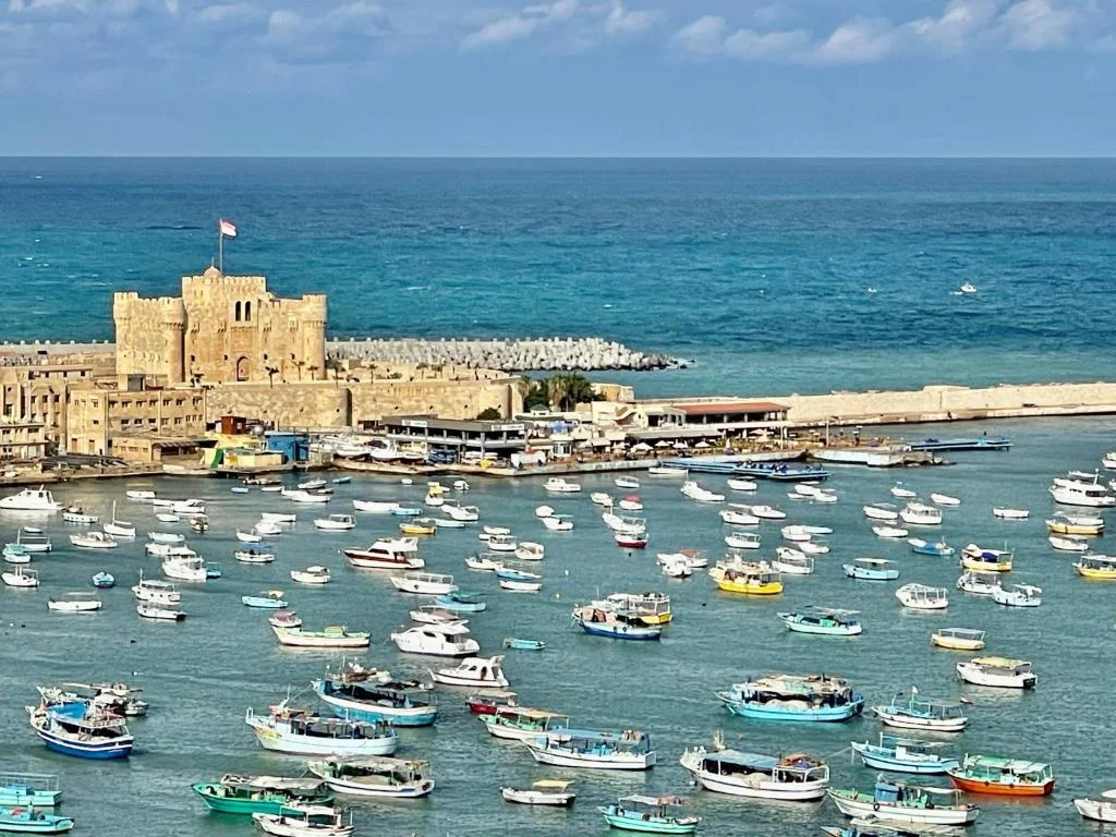 Elevated view of Alexandria's Eastern Harbour packed with fishing boats, with the Citadel of Qaitbay standing at the water's edge.