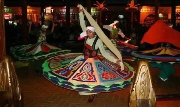 Whirling dervish performers in colorful spinning skirts perform a Tanoura dance on stage at an evening cultural show.