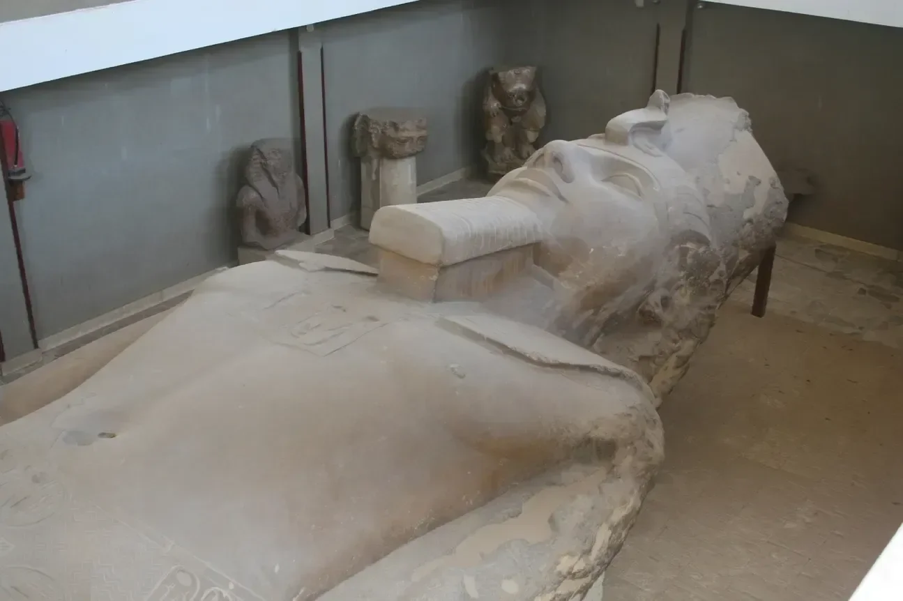 A large reclining stone statue of a pharaoh lies on display indoors, surrounded by smaller carved statues.
