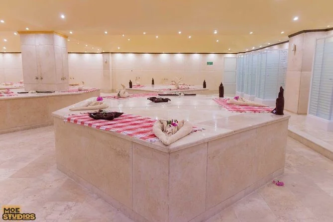 An empty hammam-style spa room with stone benches topped in red-and-white checkered towels folded into swan shapes, lit by recessed ceiling lights.