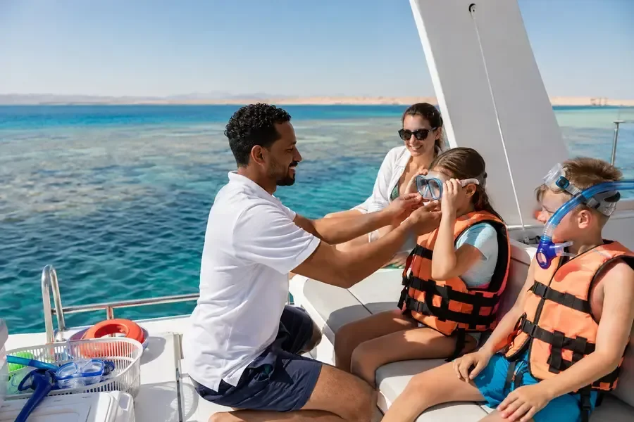 A crew member helps a young girl put on a snorkel mask while her brother and mother look on aboard a private boat.