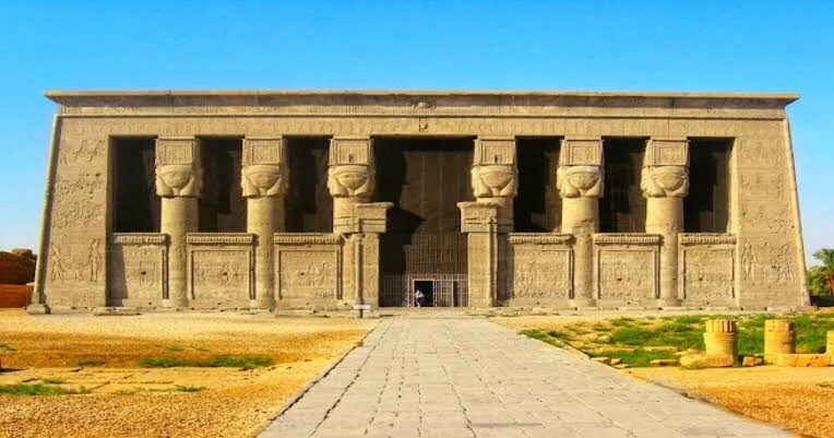 Kamenná cesta vede k monumentální fasádě chrámu Dendera s řadami sloupů s hlavicemi bohyně Hathor.
