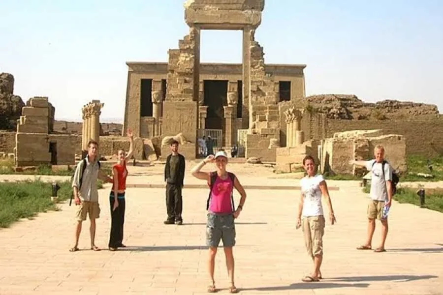 Šest turistů pózuje a mává před rozpadlou kamennou branou vstupu do chrámu.