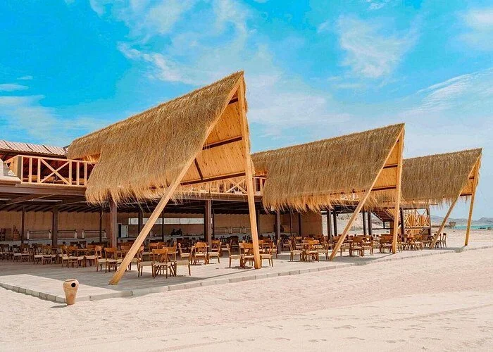 Triangular thatched-roof pavilions housing an open-air restaurant with wooden tables and chairs on the beach.