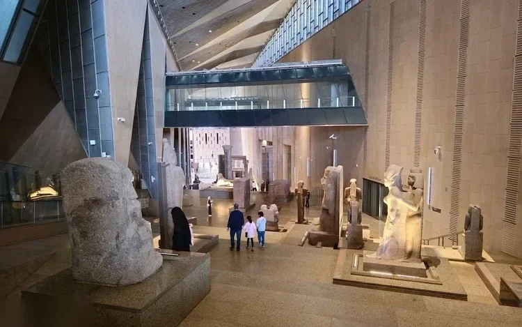 Grand hall of the Grand Egyptian Museum with rows of ancient stone statues and visitors walking past.