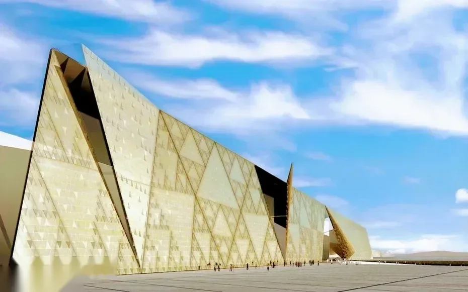 Exterior view of the Grand Egyptian Museum's angular golden stone facade against a blue sky.