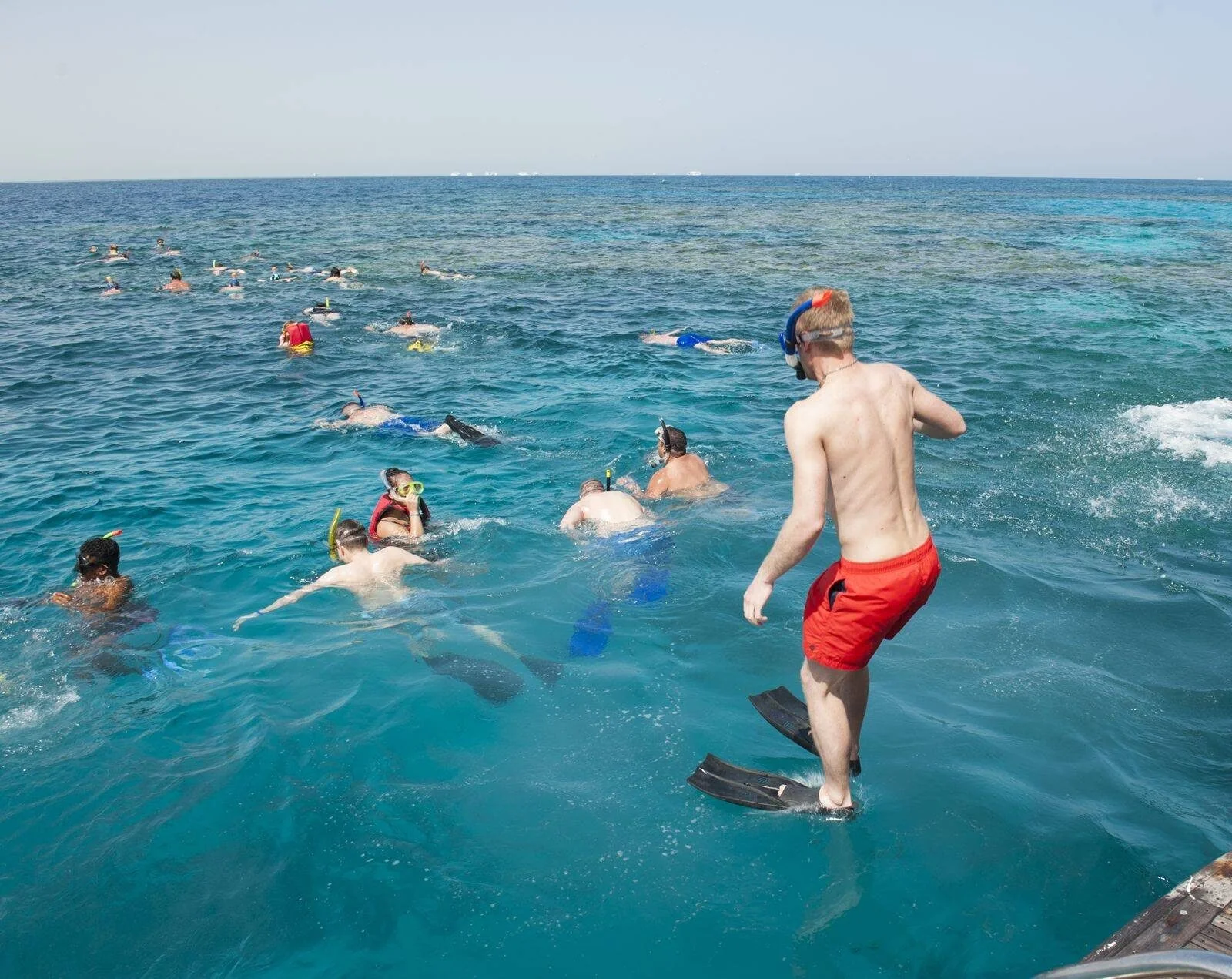 Snorkeler stepping off the back of a boat into the sea to join a group already swimming over the reef.
