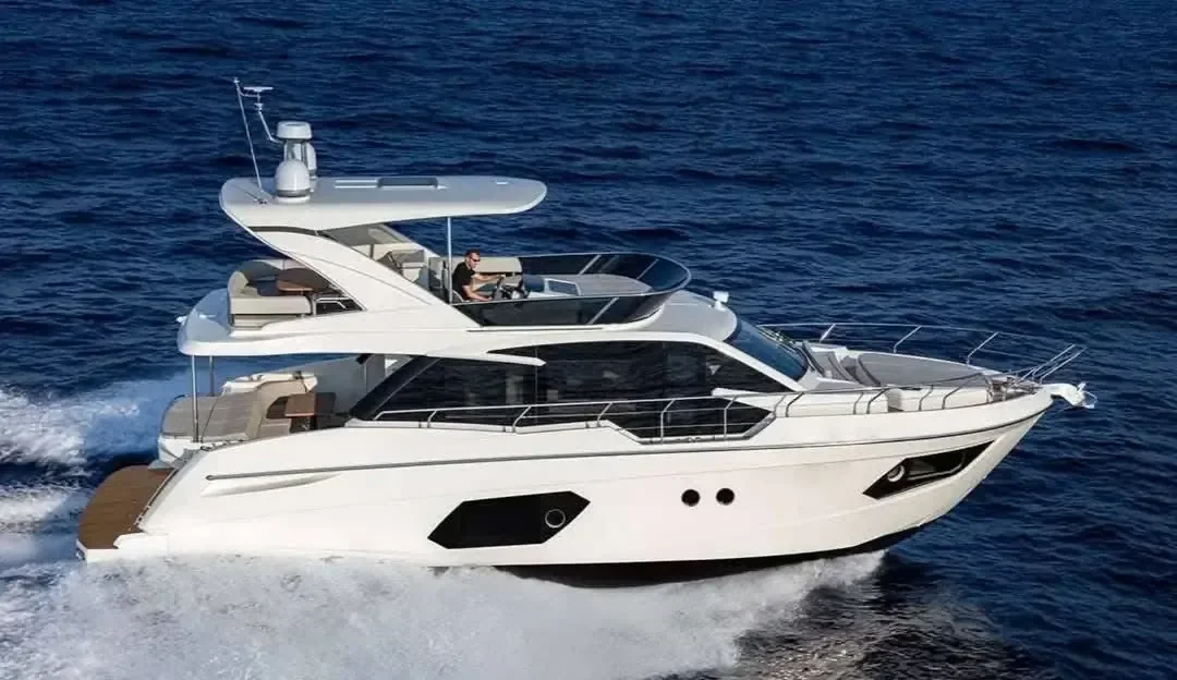 Luxury motor yacht cruising at speed viewed from above, with a person driving from the open flybridge.