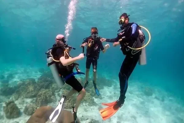 Three scuba divers hovering underwater above a reef, one giving hand signals to the group.