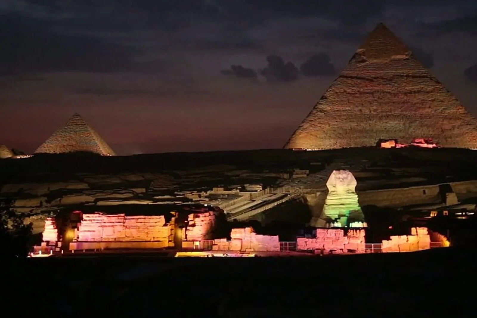 Two illuminated pyramids and the Sphinx at night under a starry sky, with faint overlaid text across the image.