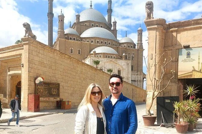 A couple posing on a stone ramp with the domed Muhammad Ali Mosque and stone lion statues in the background.