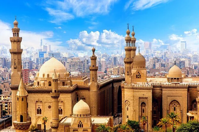 An aerial view of the domed and minaret-topped mosques of the Citadel rising above the dense Cairo skyline.