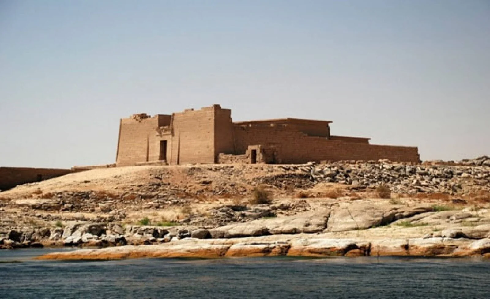 A sandstone temple with a tall pylon standing on a rocky island, viewed across the waters of Lake Nasser.