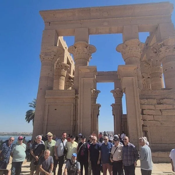 A large group of tourists posing beneath a papyrus-column stone kiosk with tall carved capitals.