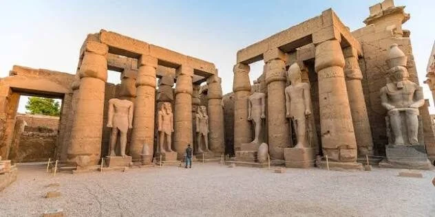 Colossal statues of Ramesses II stand among towering papyrus columns in the peristyle court of Luxor Temple.