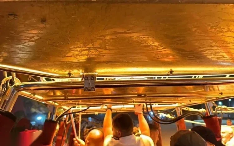 A gold-lit view looking up inside a hot air balloon basket, with passengers holding onto ropes as the burner glows overhead.