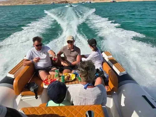 A small group enjoys a seated snack aboard a speedboat leaving a foaming wake, with two more boats visible in the distance.