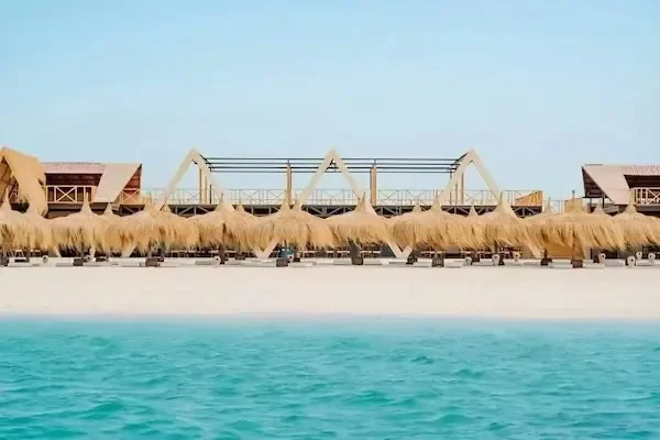 Row of thatched-roof beach huts seen from the water with turquoise sea in the foreground.