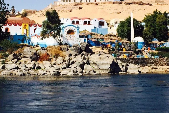 View from the Nile of a colorful Nubian village built into a rocky hillside, with domed white and blue buildings.