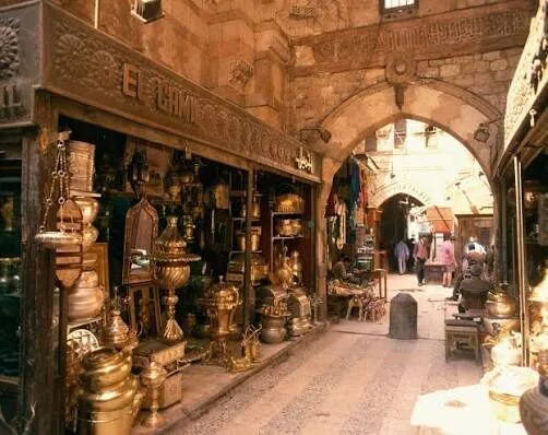A brass and copper antiques shop opens onto a stone archway passage in the Khan el-Khalili bazaar.
