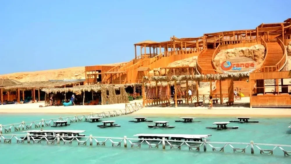 Orange Bay's wooden beach resort buildings on Giftun Island, with floating tables set in shallow turquoise water in front.