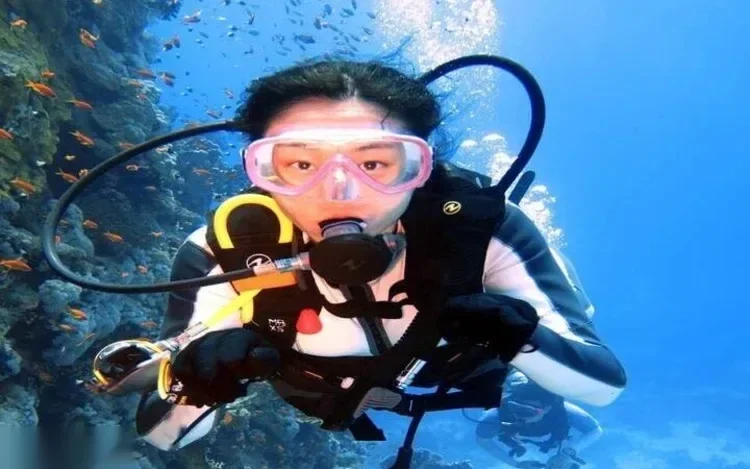 Close-up portrait of a diver in a pink mask hovering beside a coral reef with orange anthias fish.