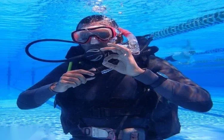 A diver gives an OK hand sign underwater in a swimming pool during training.