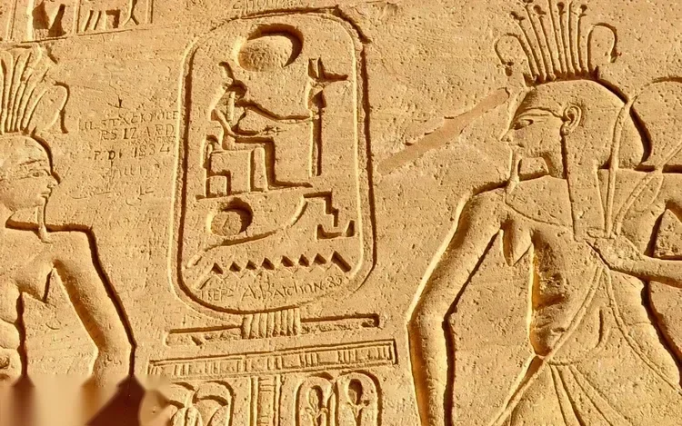 Close-up of a carved hieroglyphic cartouche and figures on a sandstone wall at Abu Simbel, worn by time.