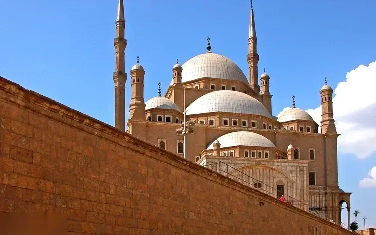 Courtyard of the Mohamed Ali Mosque with its central ablution fountain and twin minarets rising against a partly cloudy sky.