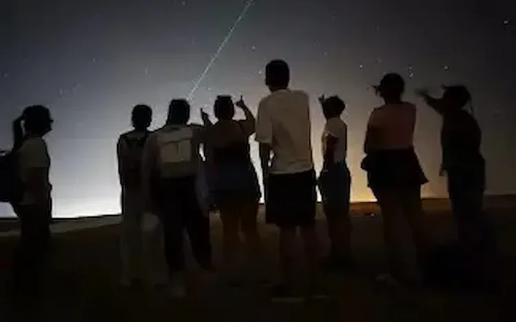 Silhouetted group of people standing together looking up at a starry night sky with a bright meteor streak.