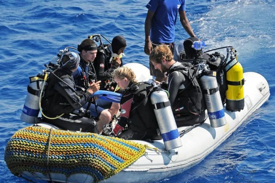 Group of scuba divers sitting in an inflatable boat getting ready to enter the water.