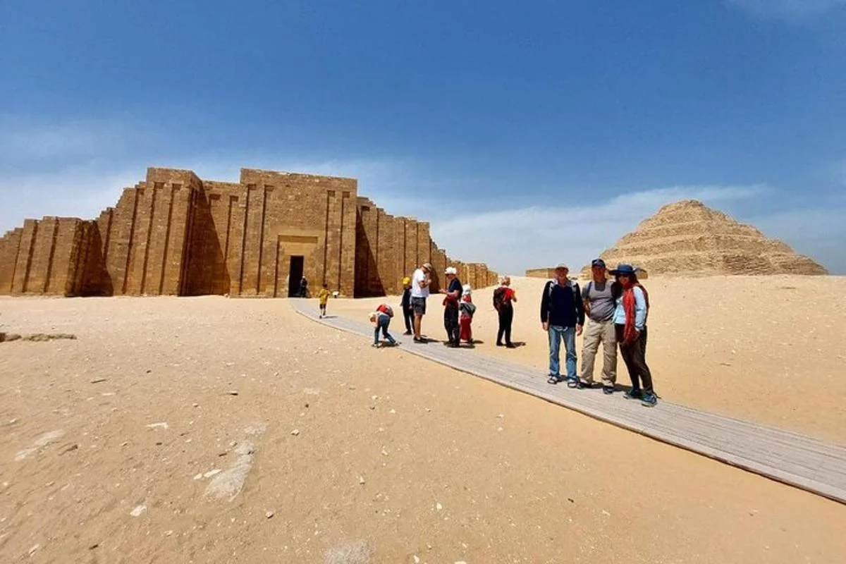 Tourists walking a wooden boardwalk toward Djoser's funerary complex with the Step Pyramid rising in the background