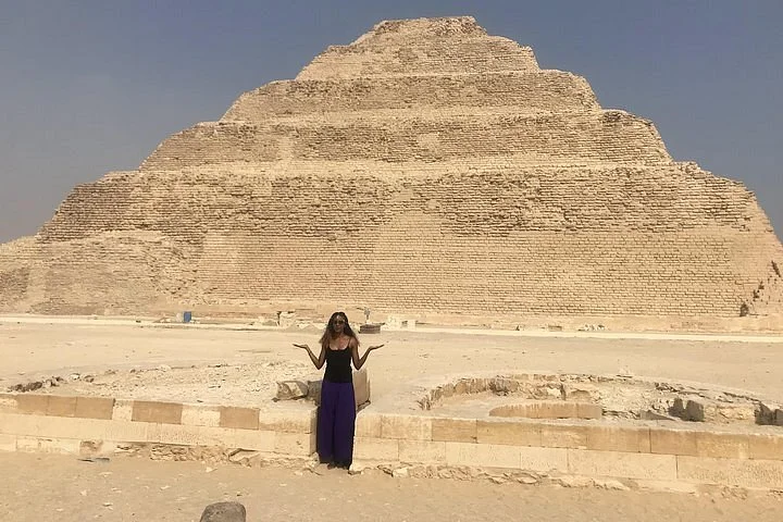 Woman posing solo with arms raised in front of the Step Pyramid of Djoser at Saqqara