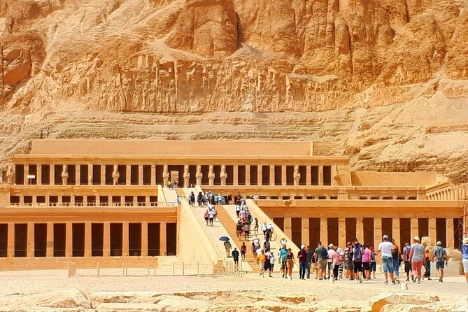 Wide view of the Temple of Hatshepsut with tourists climbing the ramps between its terraced colonnades.