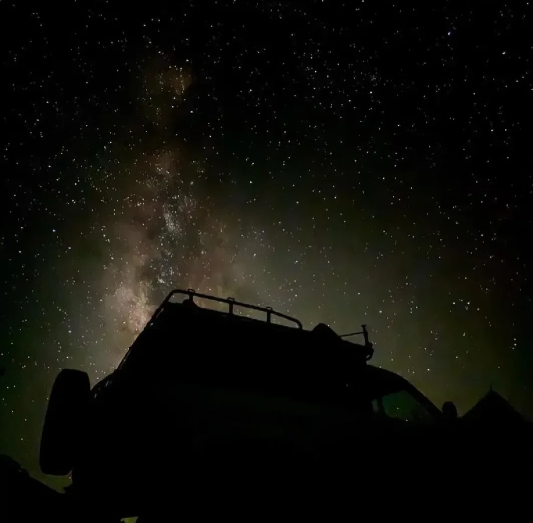 Silhouette of a 4x4 roof rack against a night sky thick with stars and the visible Milky Way band.