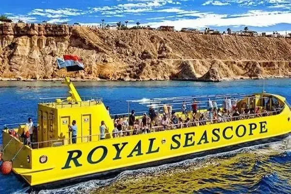 Royal Seascope boat with Egyptian flag cruising past a dramatic reddish rocky coastline under a partly cloudy sky