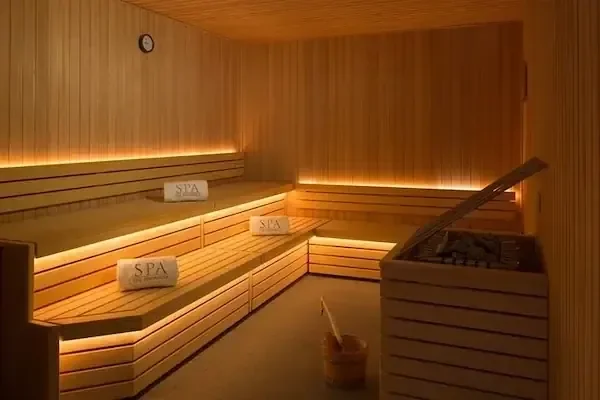 Empty wooden sauna interior with three rolled white 'Spa' towels on the benches and a bucket of water beside the stove