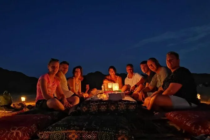 Group of guests seated on cushions around a low table with candles and snacks under a dark starry desert sky