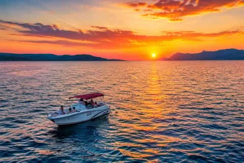 Aerial view of a small canopied speedboat with passengers cruising toward a vivid orange sunset