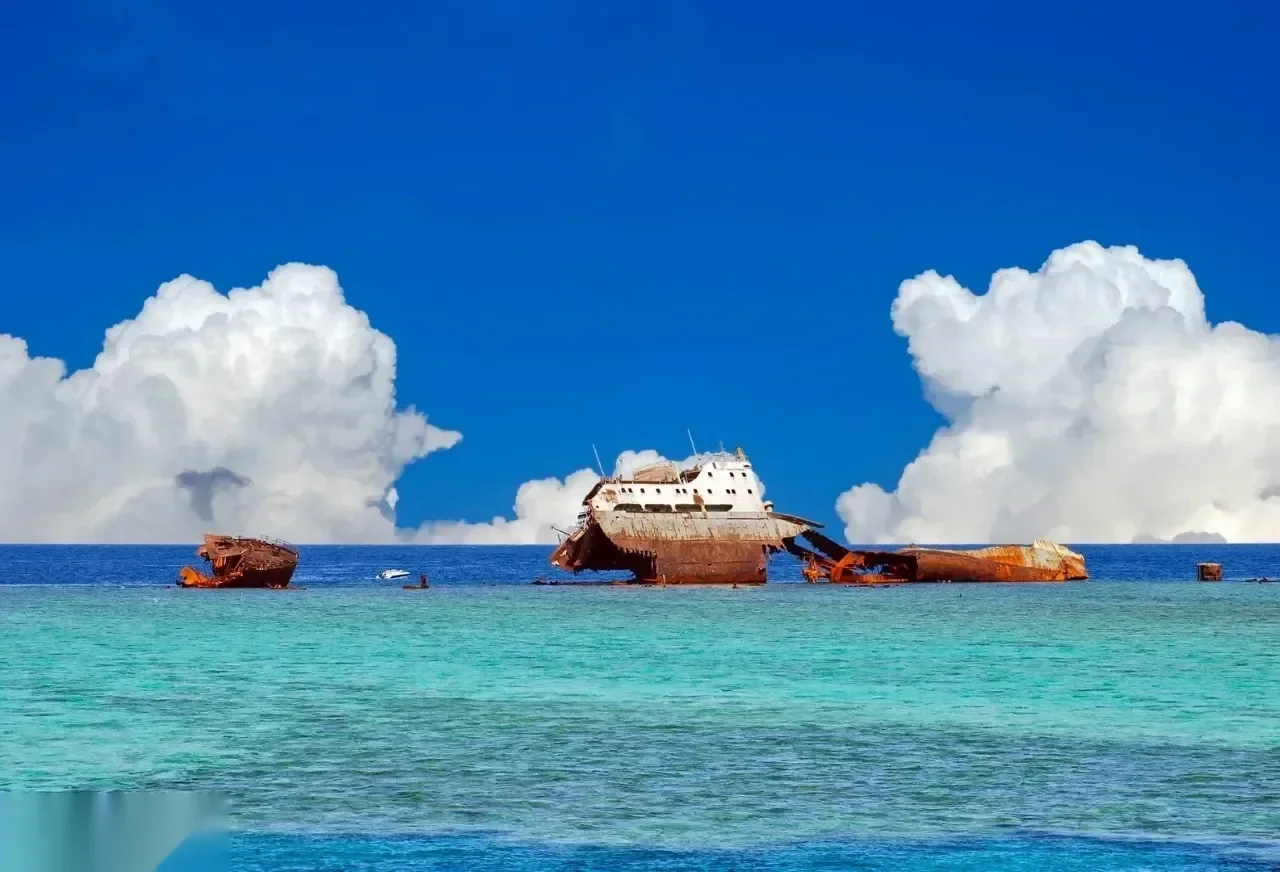 Large rusted cargo shipwreck broken apart on a reef under a dramatic sky with towering cumulus clouds