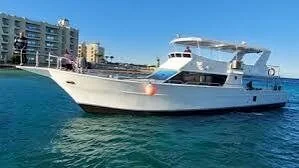 Small white motor yacht docked near a beachfront hotel building, calm turquoise water in the foreground
