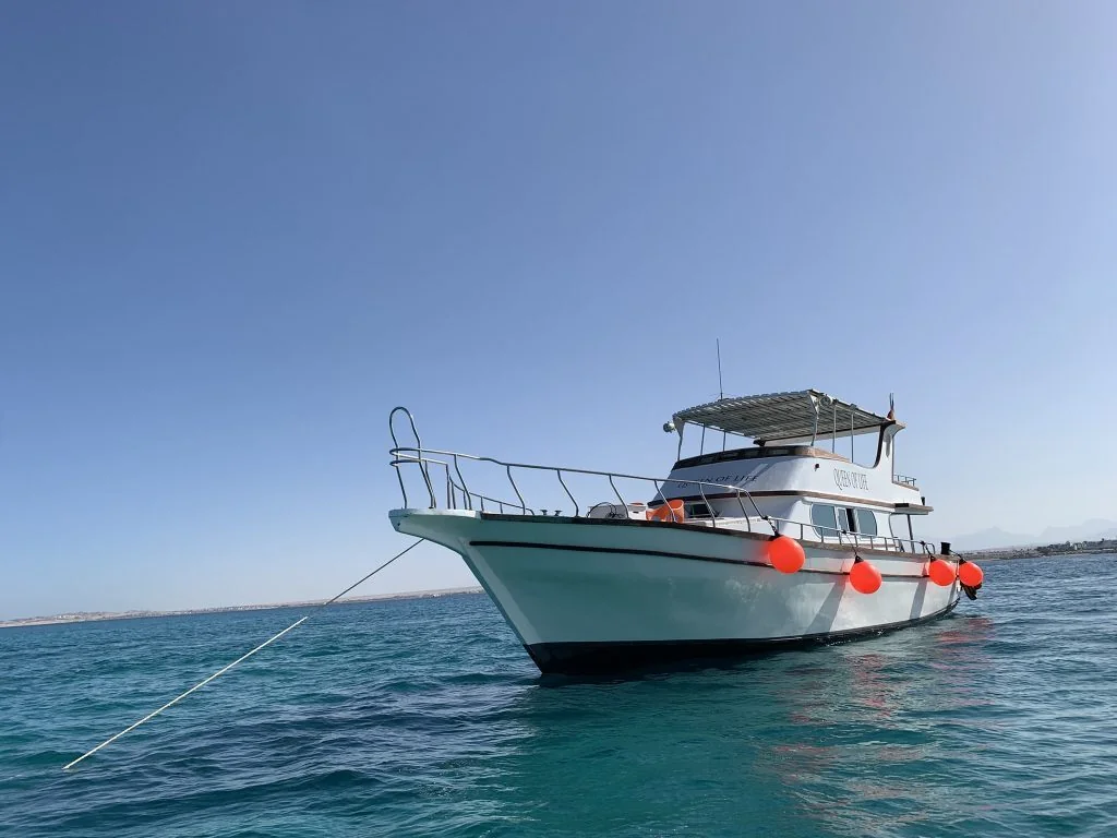 White motor yacht 'Queen of Tut' with orange fenders anchored in turquoise water near the Hurghada coast