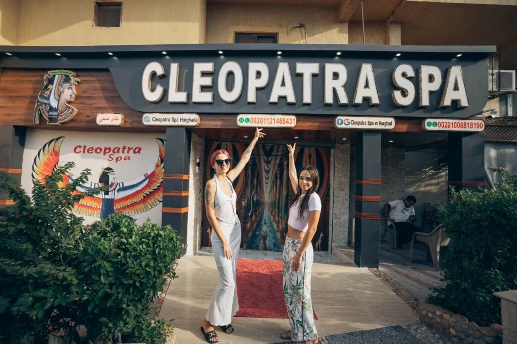 Storefront signage reading 'Cleopatra Spa' with two women posing outside the entrance, Egyptian-themed mural art on the wall
