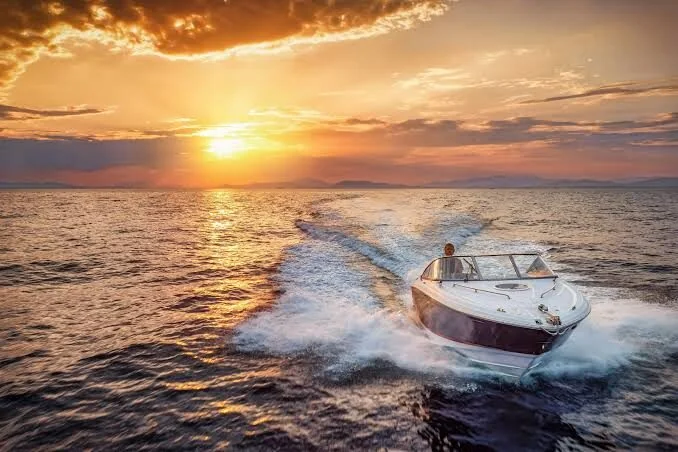 Speedboat cutting through dark water at sunset with dramatic orange and gold clouds filling the sky
