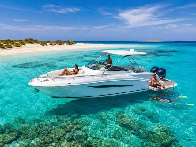 Bowrider motorboat anchored near a sandy island with a woman sunbathing on deck and a man snorkeling off the swim platform in bright turquoise water