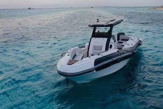 White speedboat with a black canopy top drifting on calm turquoise water with distant boats on the horizon