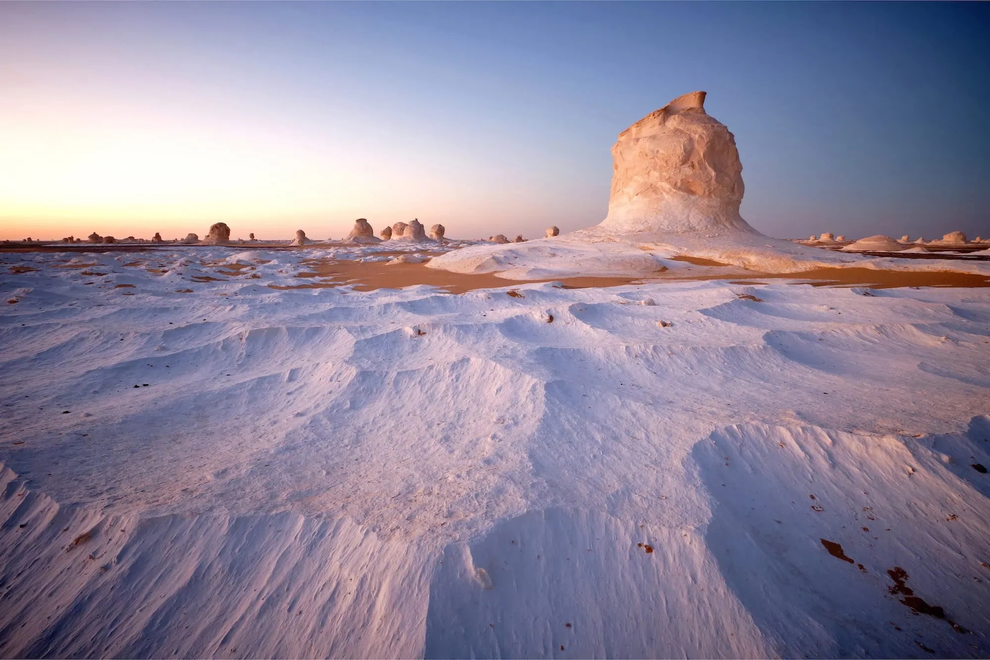 Large solitary chalk rock pinnacle rising from rippled white sand at sunrise